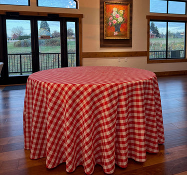 Red and white checkered tablecloth on a wooden table with a painting on the wall.
